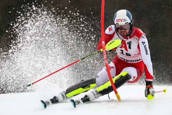Slalomfahrer in Großaufnahme vor der Stange, Schnee spritzt.