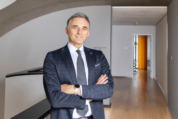 Ein Mann mit blau kariertem Anzug und weißem Hemd lächelt in die Kamera