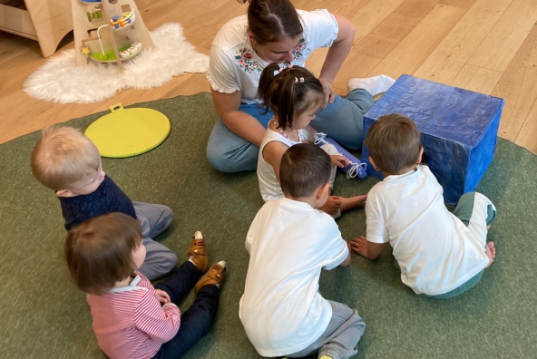 Eine Frau und mehrere Kinder sitzen auf einem Fußboden und spielen