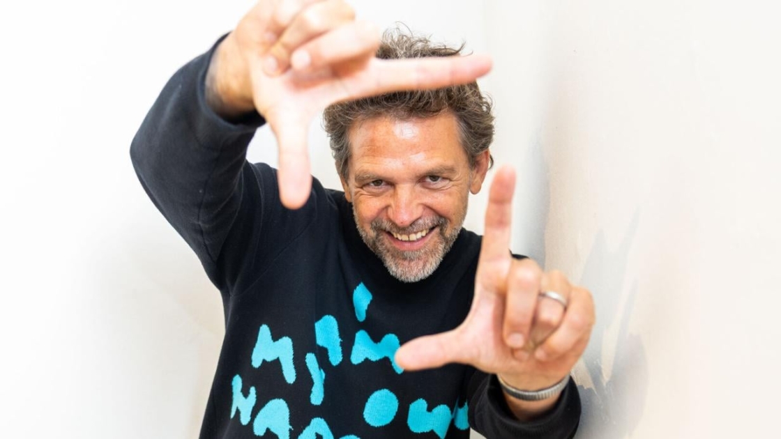 Der Künstler Rainer Hosch steht vor der Kamera und trägt einen schwarzen Pullover mit Schriftzug
