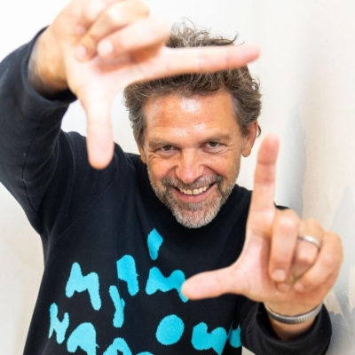 Der Künstler Rainer Hosch steht vor der Kamera und trägt einen schwarzen Pullover mit Schriftzug