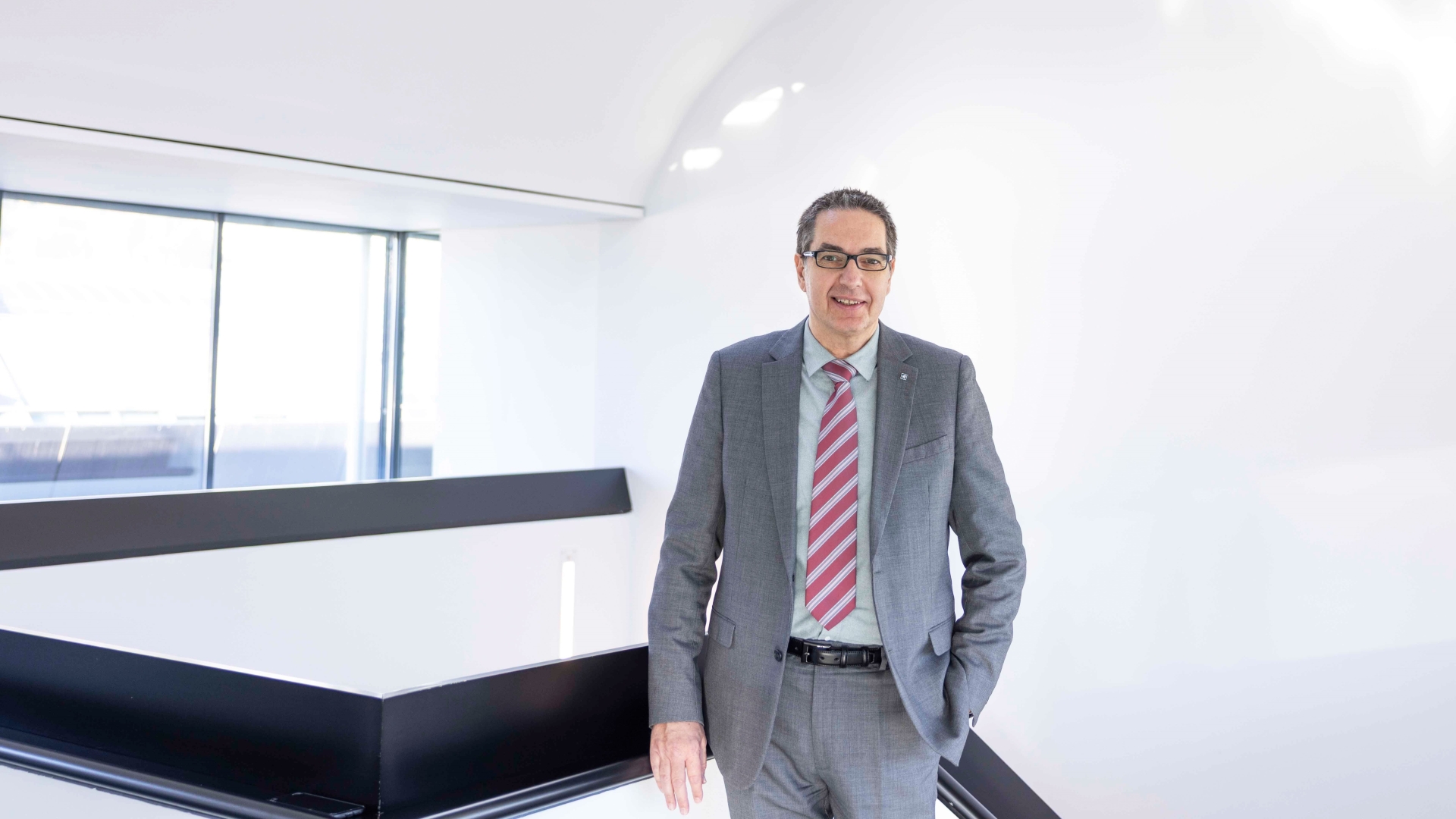 Ein Mann mit Brille in grauem Anzug und mit gestreifter Krawatte lächelt in die Kamera