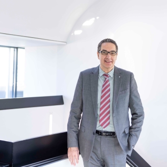 Ein Mann mit Brille in grauem Anzug und mit gestreifter Krawatte lächelt in die Kamera