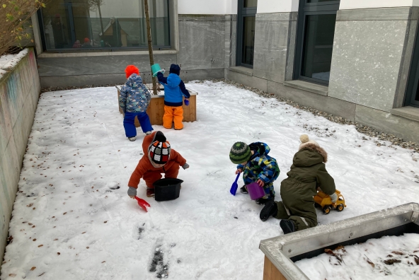 Kinder spielen im Schnee mit kleinen Schaufeln und Kübeln