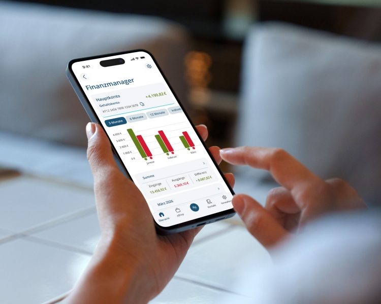Hände halten ein Smartphone, auf dem Finanzmanager geschrieben steht und Balkendiagramme abgebildet sind. In der Funktion können Zeiträume ausgewählt werden und man hat eine Übersicht über die Zahlungseingänge und Ausgänge des Hauptkontos.