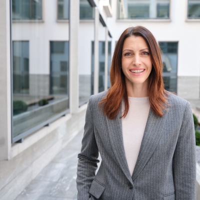Skeletonfahrerin Janine Flock trägt einen grauen Anzug und steht im Innenhof der BTV Vier Länder Bank AG in Innsbruck. Sie blickt in die Kamera, umgeben von modernen Gebäudeelementen.