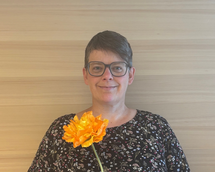 Eine Frau in einem geblümten Kleid hält eine gelbe Blume in der Hand.