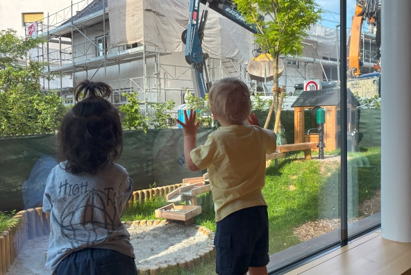 Zwei Kinder schauen aus einem Fenster und beobachten ein Gebäude, das gerade umgebaut wird.