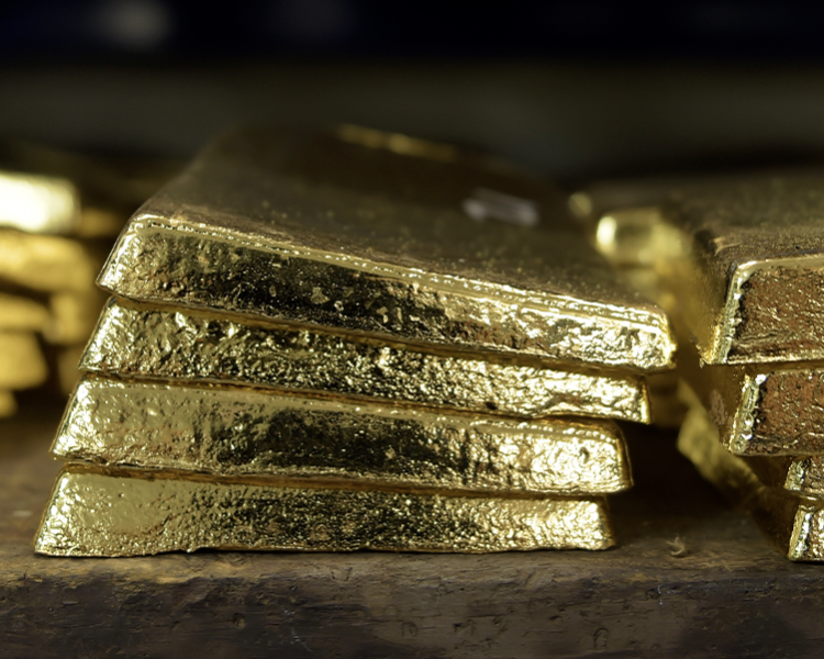 Ein Stapel glänzender Goldbarren liegt ordentlich auf einem Holzbrett.