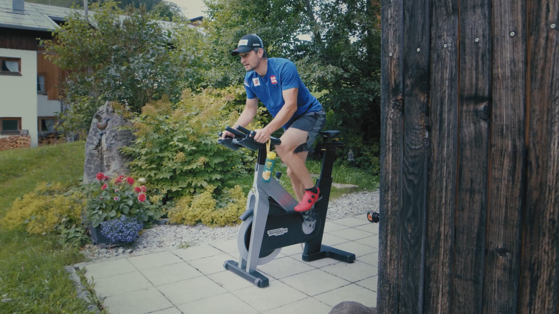 Skirennfahrer Johannes Strolz trainiert auf einem Hometrainer auf einer Terrasse.