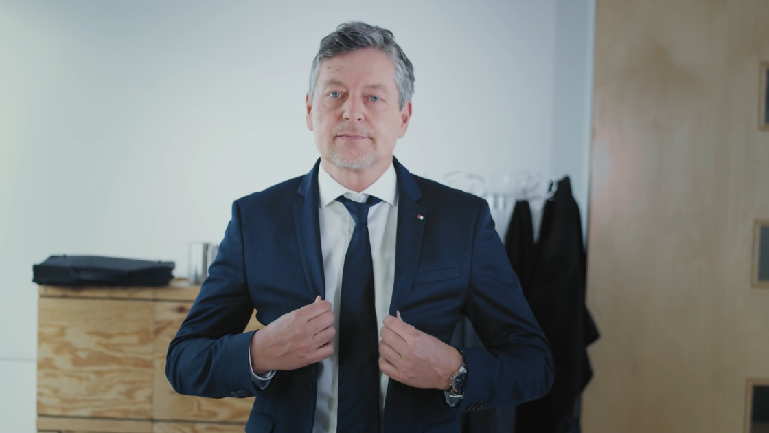 Ein Mann in einem dunklen Anzug mit BTV‑Logo und BTV‑Pinnadel steht frontal zur Kamera und blickt direkt hinein.