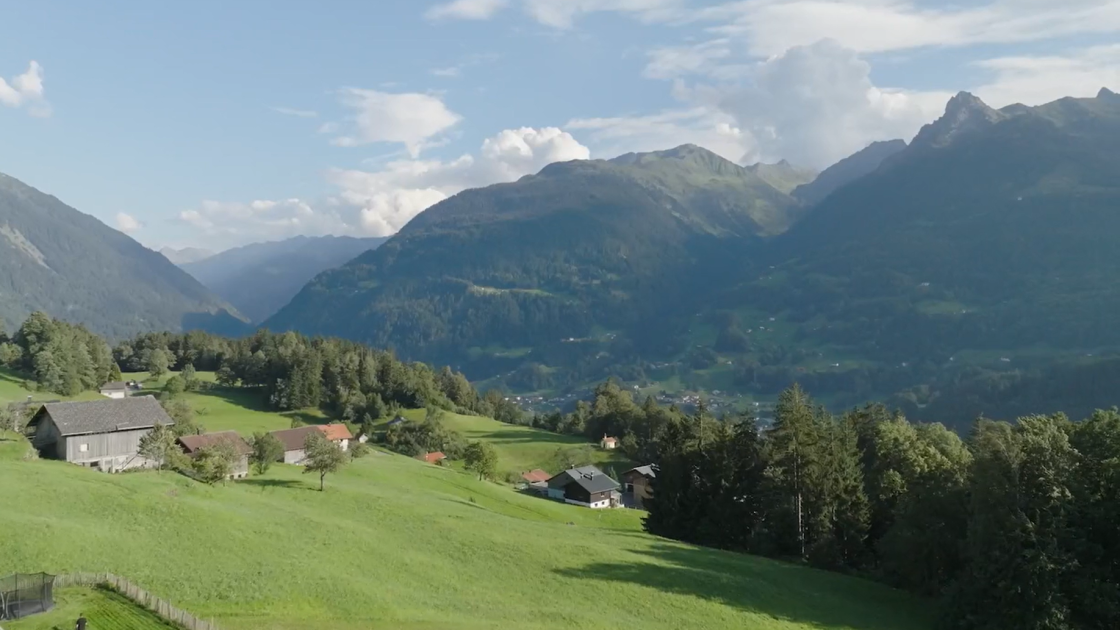 „Aussicht über ein weites Alpental mit Bergen, Wiesen und klarer Fernsicht.
