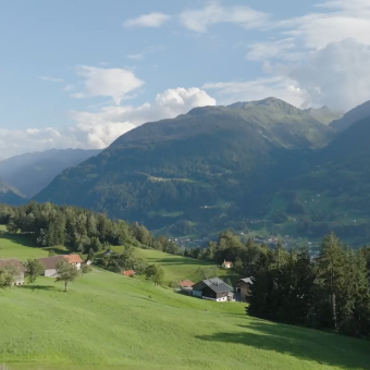 „Aussicht über ein weites Alpental mit Bergen, Wiesen und klarer Fernsicht.