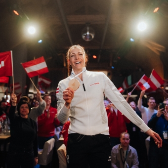 Skeletonpilotin Janine Flock jubelt nach ihrem Olympiasieg und hält ihre Goldmedaille, umgeben von einer begeisterten Menschenmenge