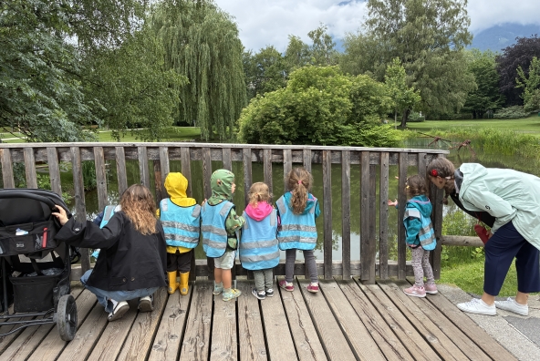 Kinder und eine Begleitperson der MUKKI‑Kinderkrippe beobachten gemeinsam einen Teich im Innsbrucker Sillpark und schauen aufmerksam auf das Wasser und seine Umgebung.