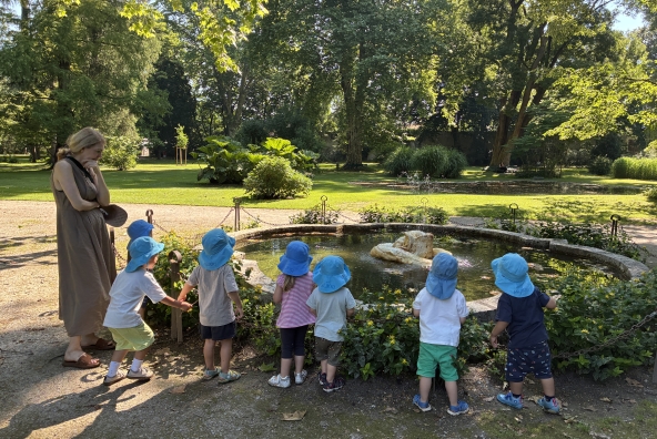 Kinder der MUKKI‑Kinderkrippe betrachten gemeinsam einen Teich im Innsbrucker Hofgarten und beobachten interessiert das Wasser und seine Umgebung.