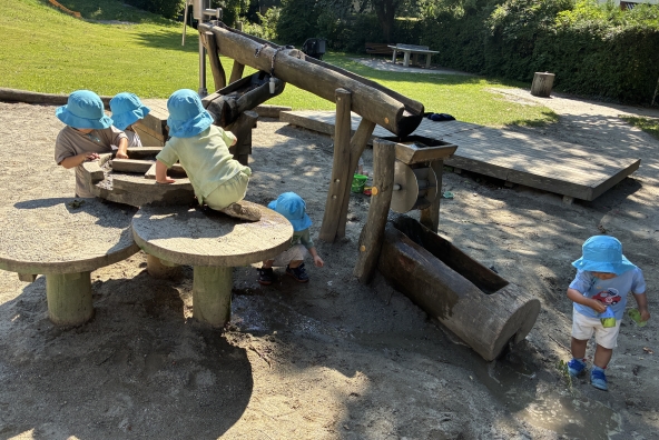 Kinder der MUKKI‑Kinderkrippe spielen auf einem Spielplatz mit Wasser.
