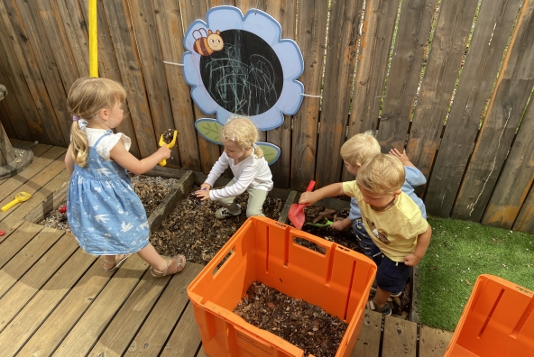 Kinder der MUKKI‑Kinderkrippe spielen gemeinsam mit Erde und kleinen Plastikbehältern und erkunden dabei Materialien und Formen.