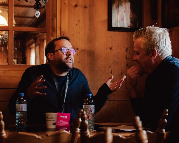 Paul Ronzheimer diskutiert beim versus Festival 2026 engagiert ein Thema mit einem Kollegen an einem Tisch sitzend.