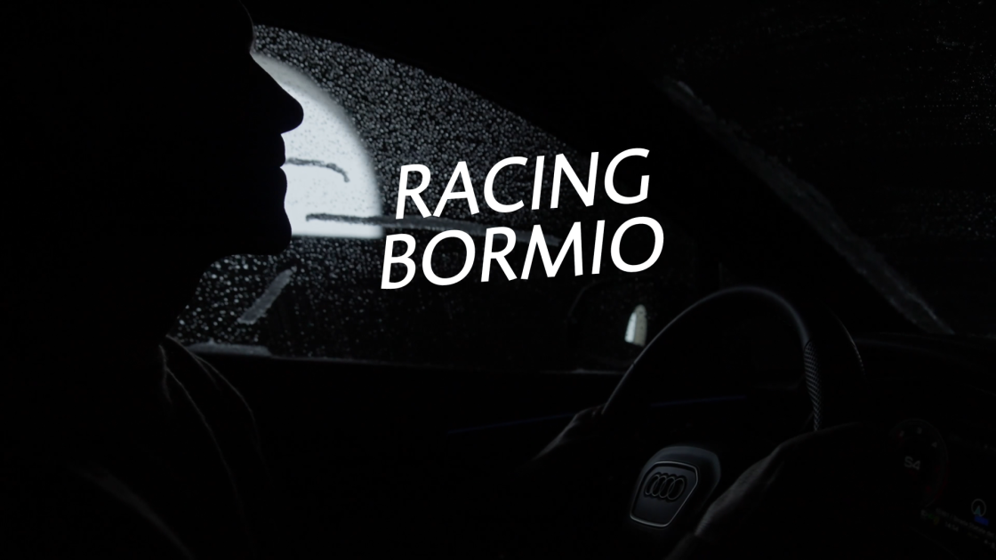 Ein schwarz‑weißes Foto zeigt Skilegende Benni Raich, der im Auto sitzt. Im Vordergrund ist der Schriftzug „Racing Bormio“ zu sehen.