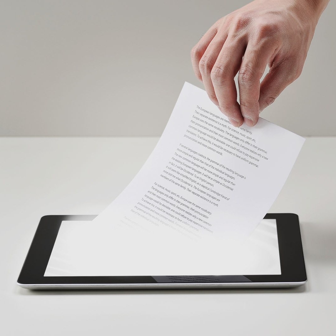 Eine Hand mit einem Blatt Papier über einem Tablet Computer