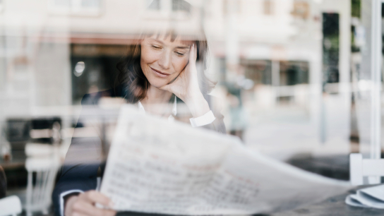 Eine Geschäftsfrau sitzt in einem Kaffeehaus und liest eine Zeitung