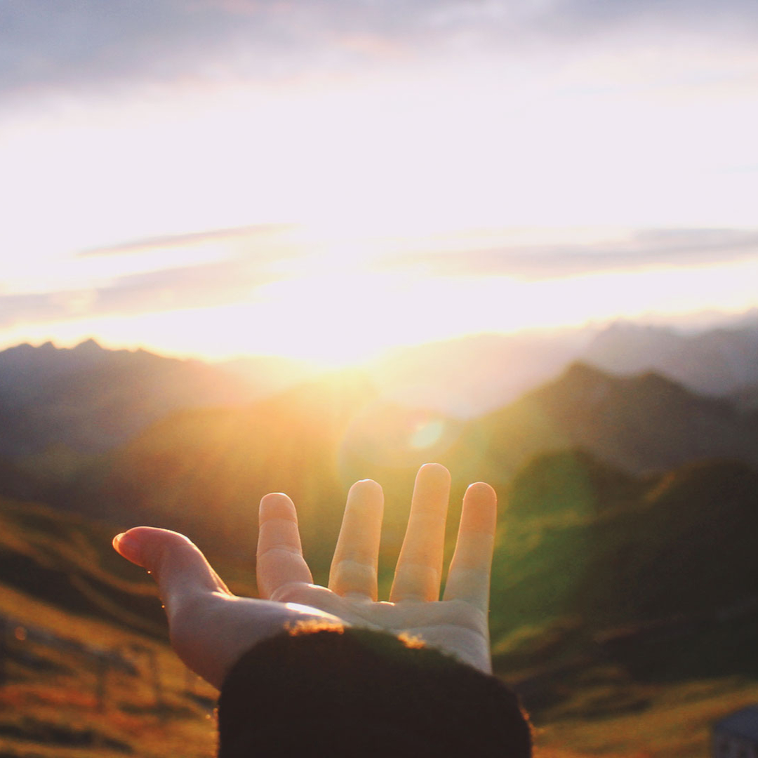 Frau streckt eine Hand in Richtung Sonnenuntergang in den Bergen