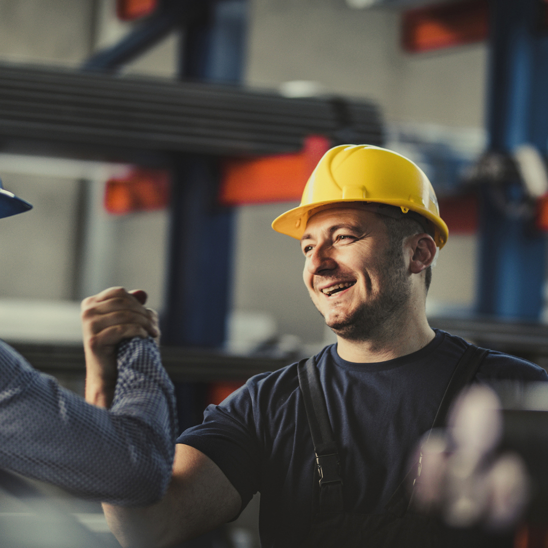 Zwei Arbeiter mit Helm begrüßen sich in Fabrikshalle