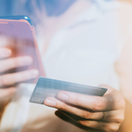 Eine Frau hält in der linken Hand eine Kreditkarte und in der rechten Hand ihr Smartphone