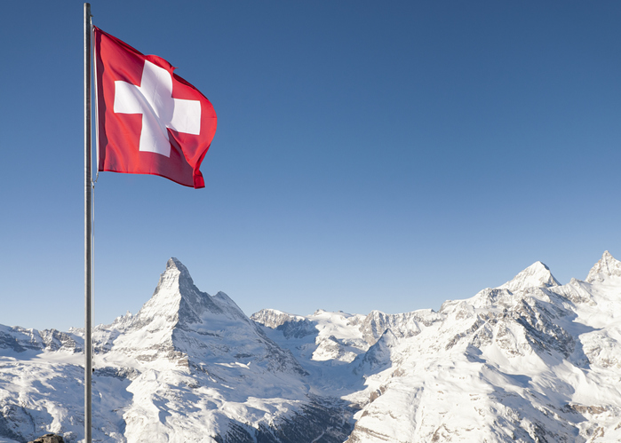 Die Schweizer Flagge weht im Wind vor einer verschneiten Bergkulisse