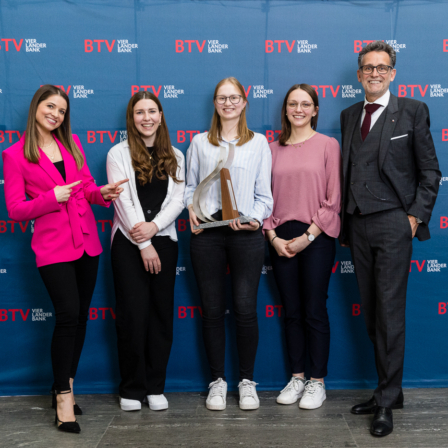 Fünf Personen in eleganter Kleidung vor einer Fotowand der BTV