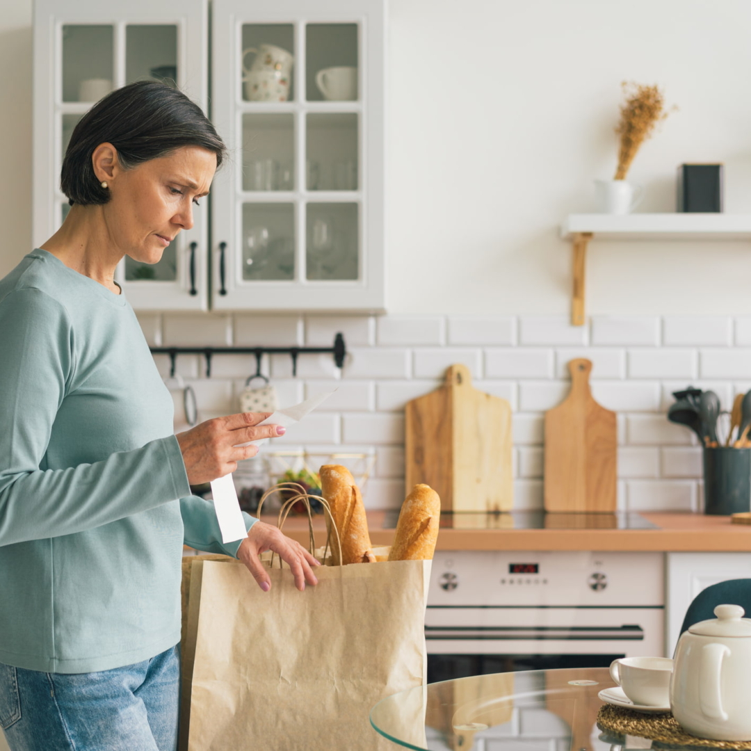 Eine Frau betrachtet frustriert den Kassabon in ihrer Küche nach dem Einkaufen im Supermarkt