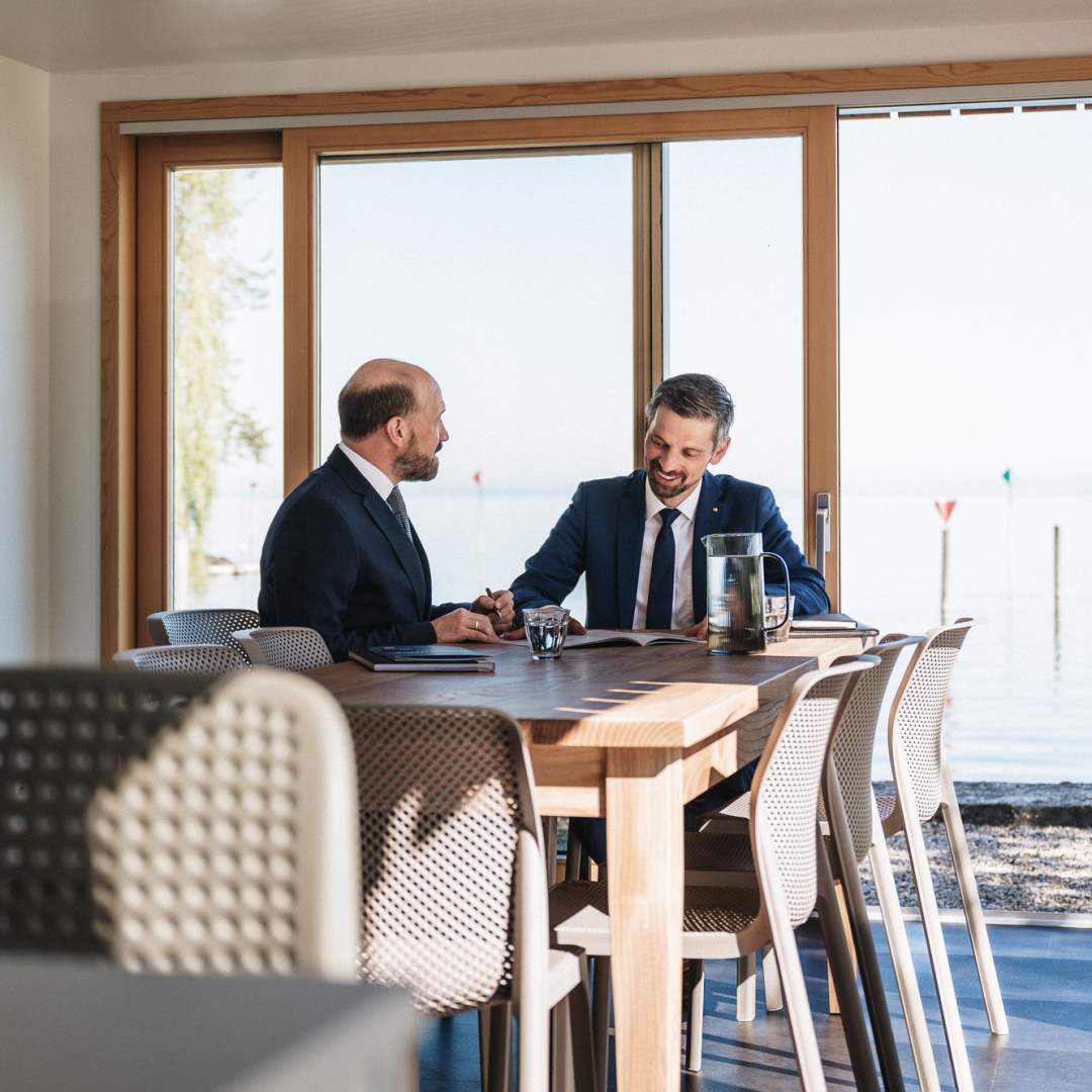 Zwei Männer im Anzug unterhalten sich an einem Esstisch.