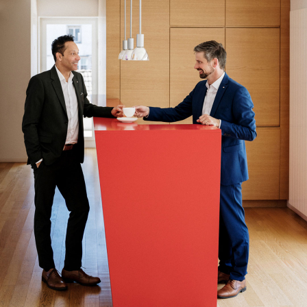 Zwei Männer unterhalten sich an einem Roten Stehtisch.