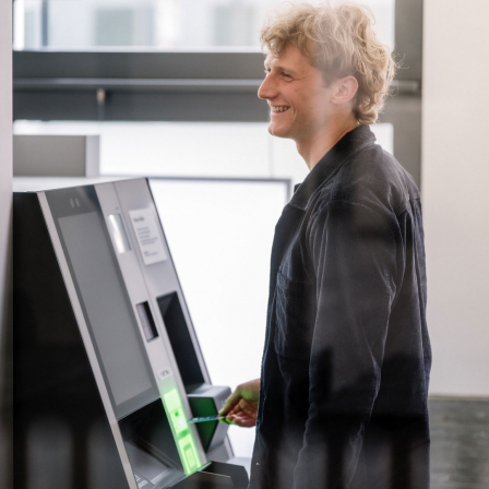 Ein Mann steht lachend an einem Geldautomaten.