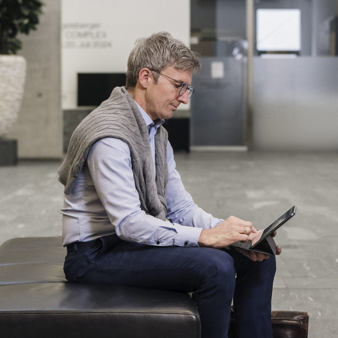 Ein Mann mit einer Brille sitzt auf einem Sessel und arbeitet mit seinem Tablet.