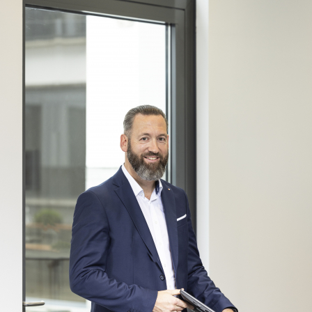 BTV Mitarbeiter Christoph Erlsbacher stehend mit Laptop vor Fenster.