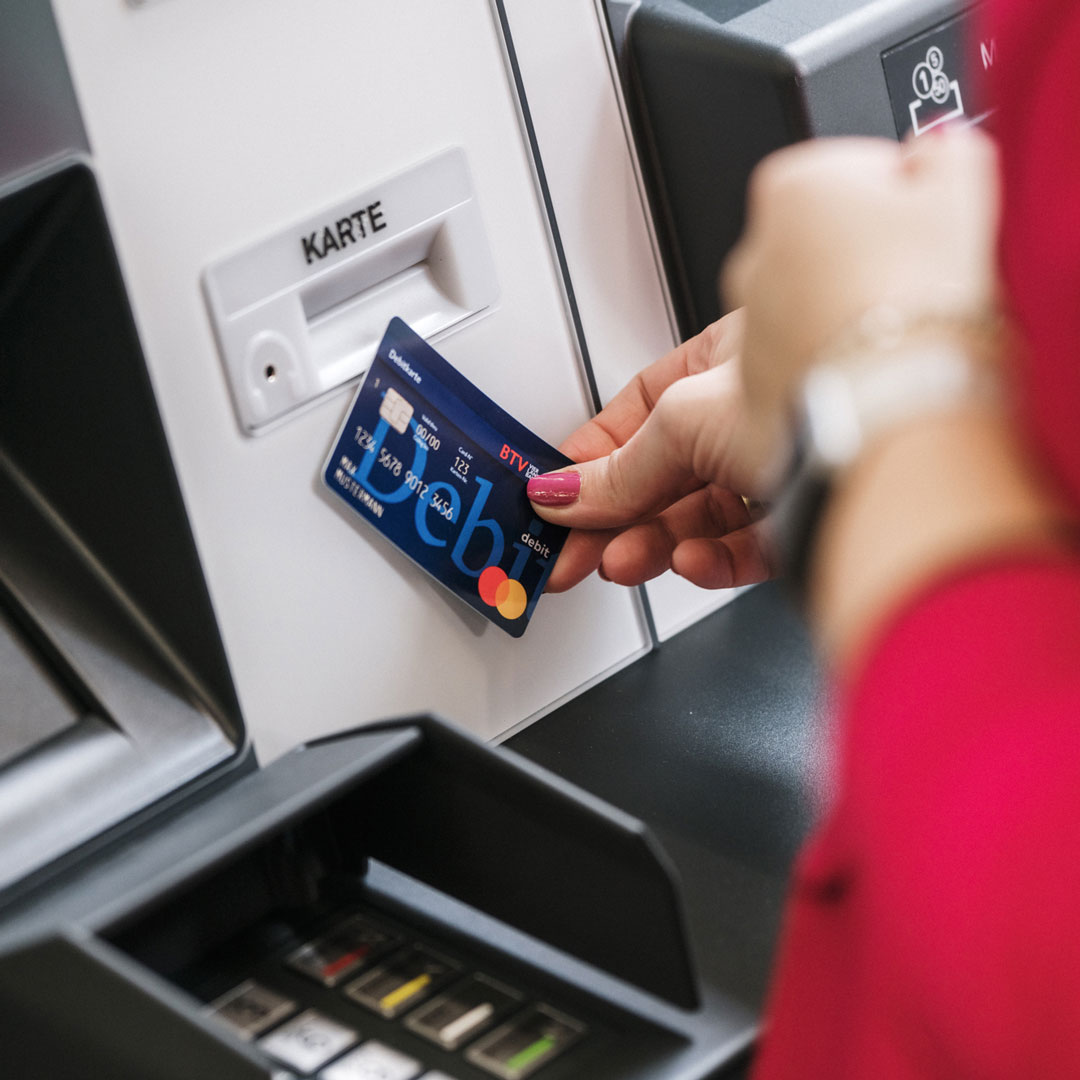 Eine Frau hält eine Debitkarte gegen einen Bankomaten.